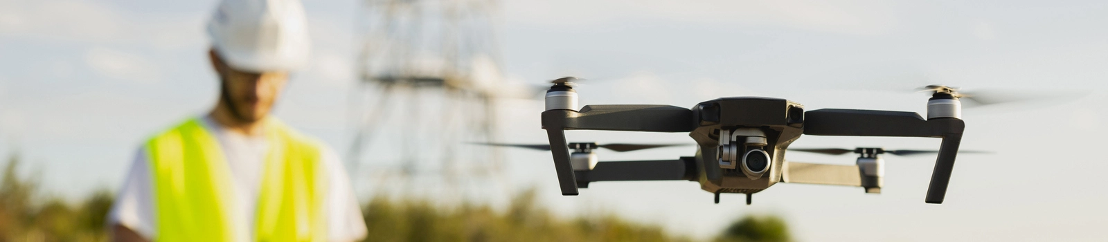 Uçan bir drone (iha) arka planda güvenlik kıyafetleriyle bir drone pilotu